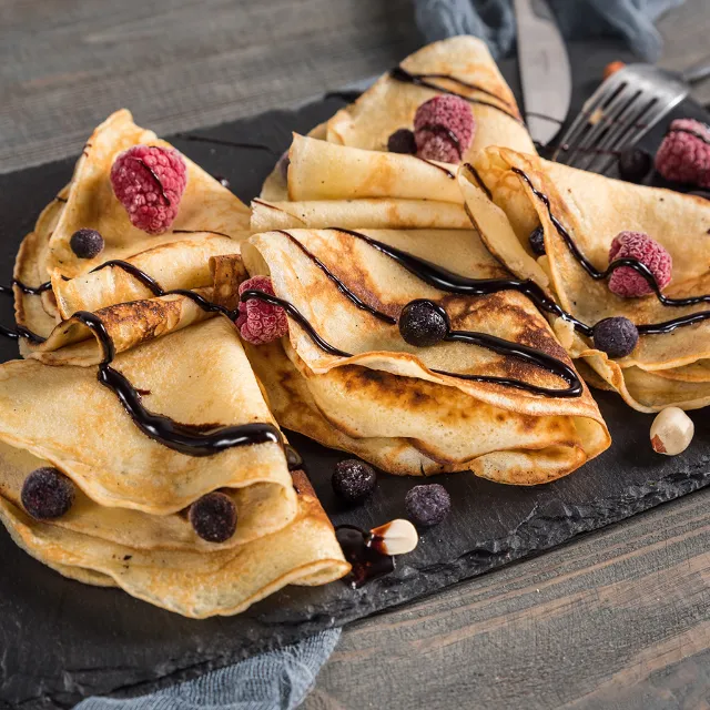 Fünf gefaltete Crêpes mit Schokoladensoße und gefrorenen Beeren auf Schieferplatte