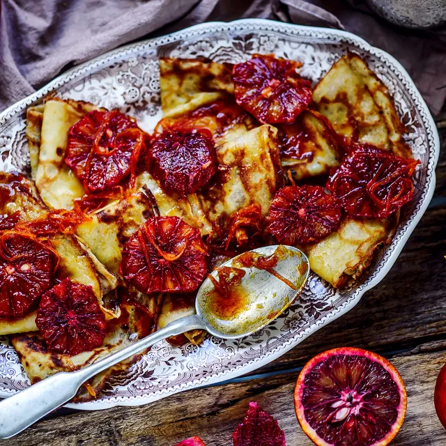 Gefaltete Crêpes mit Blutorangenscheiben und Karamellsirup auf blau-weißem Teller angerichtet